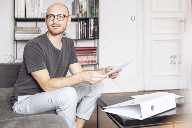 Man sitting at home on a couch holding a sheet of paper