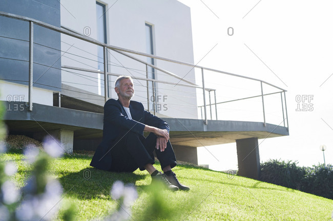 Senior businessman sitting on lawn outside a building