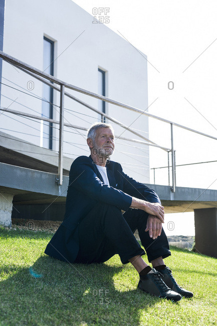 Senior businessman sitting on lawn outside a building