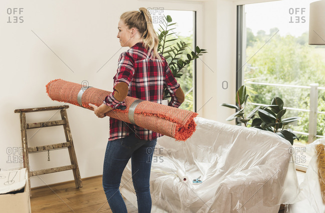 Rear view of woman moving into new home carrying carpet and potted plant