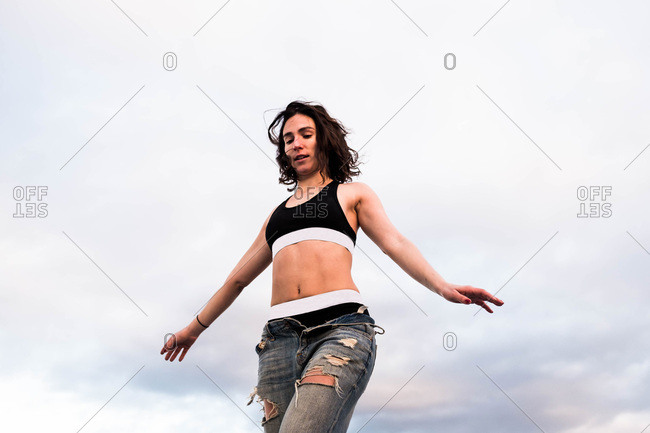 Young woman balances with sky background wearing sports bra and jeans stock  photo - OFFSET