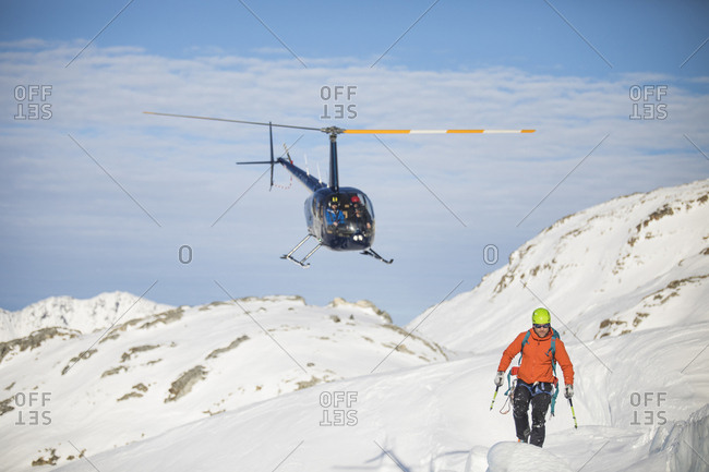 Helicopter approaches mountaineer in a snowy landscape.