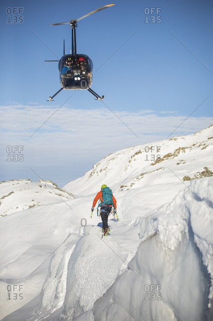 Helicopter approaches mountaineer in a mountain landscape.