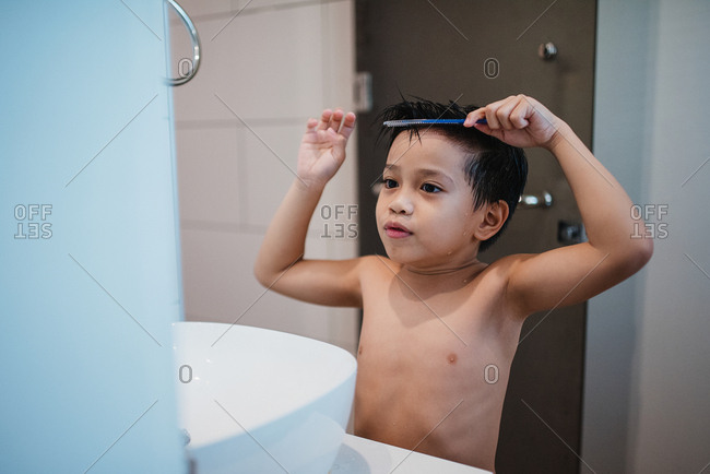 Asian boy combing hair in front of mirror