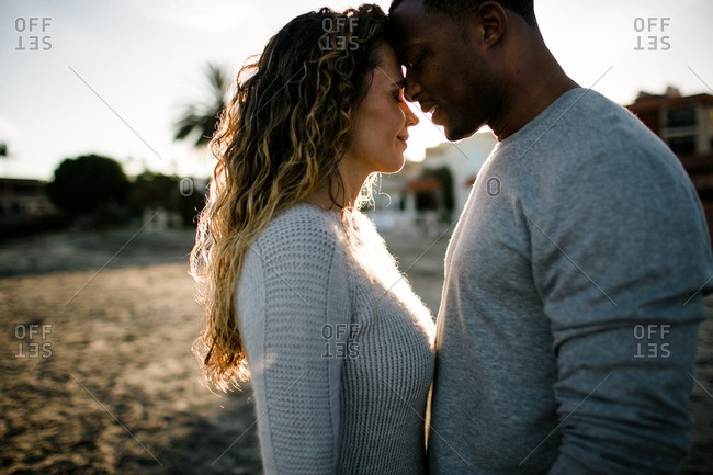 Multi racial couple embrace on beach at sunset