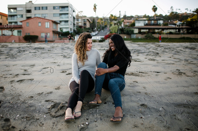 Step mom and step daughter smile at one another on beach at sunset