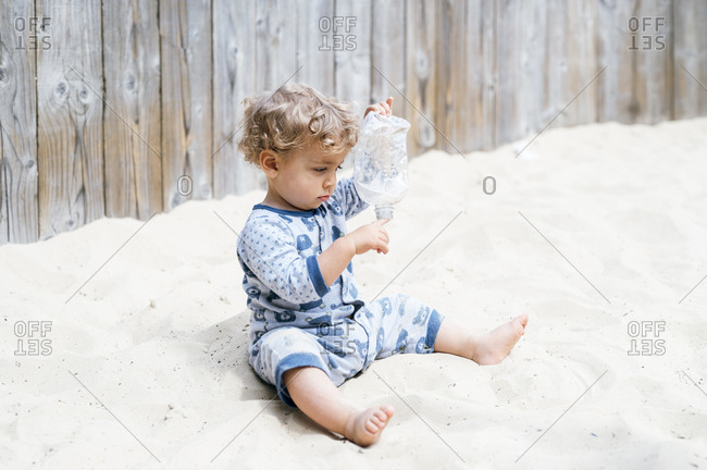 Baby boy playing with plastic bottle in sandpit