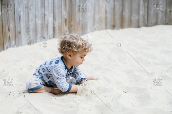 Baby boy playing alone with sand in sandpit