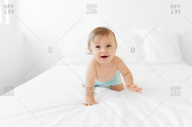 Laughing shirtless baby crawling on white bed