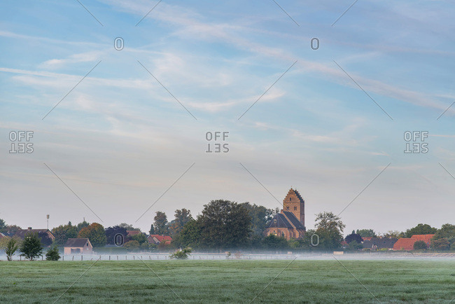 Early morning clouds over foggy field and buildings
