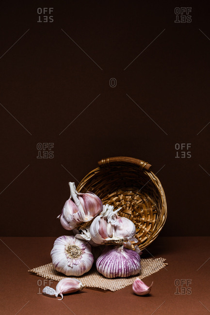 Garlic heads and wicker basket on brown background