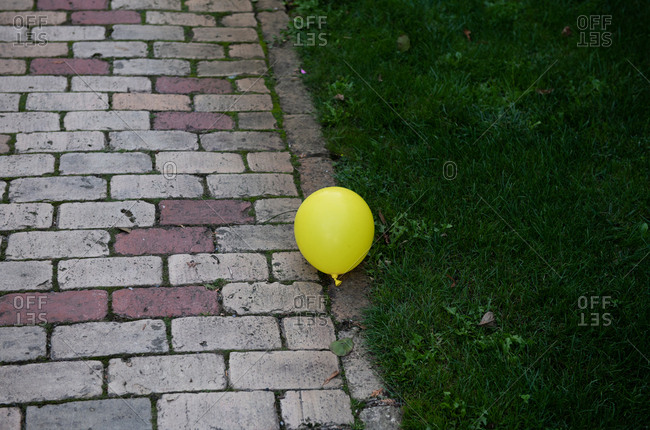 Yellow balloon floating between brick walkway and green grass