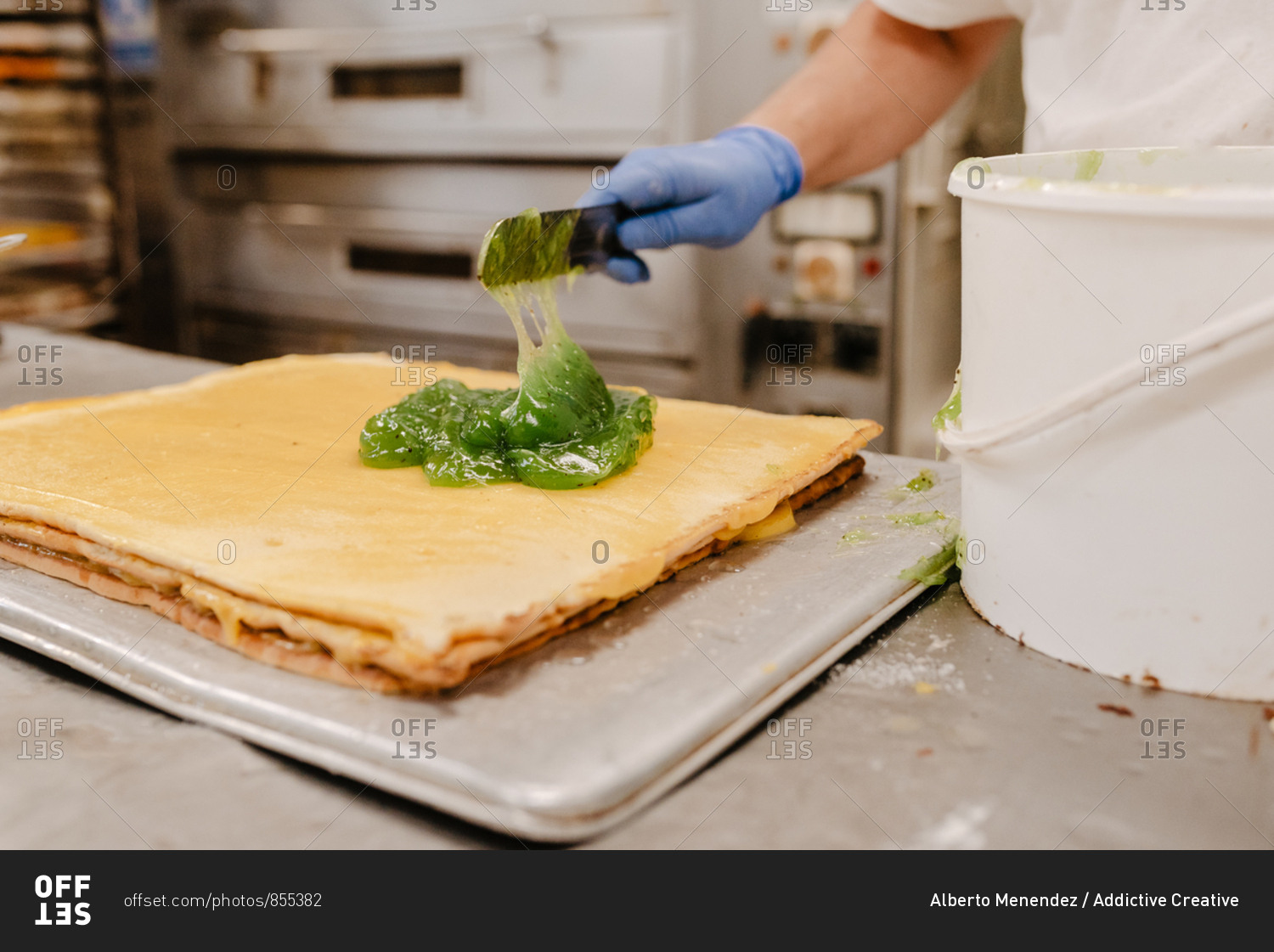 Unrecognizable confectioner putting yummy kiwi jelly from bucket on cake base while preparing pastry in bakery kitchen