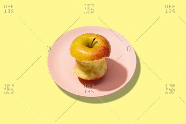 Fresh bitten apple in plate on yellow background. vibrant colorful pattern