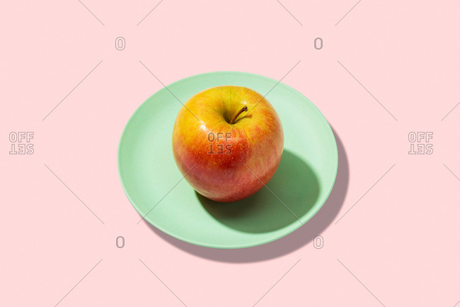 Fresh apple in plate on pink background. vibrant colorful pattern