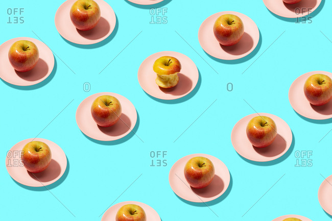 Fresh apples and bitten apple in plate on cyan background. vibrant colorful pattern