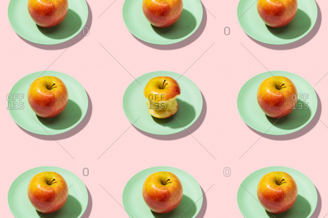 Fresh apples and bitten apple in plate on pink background. vibrant colorful pattern