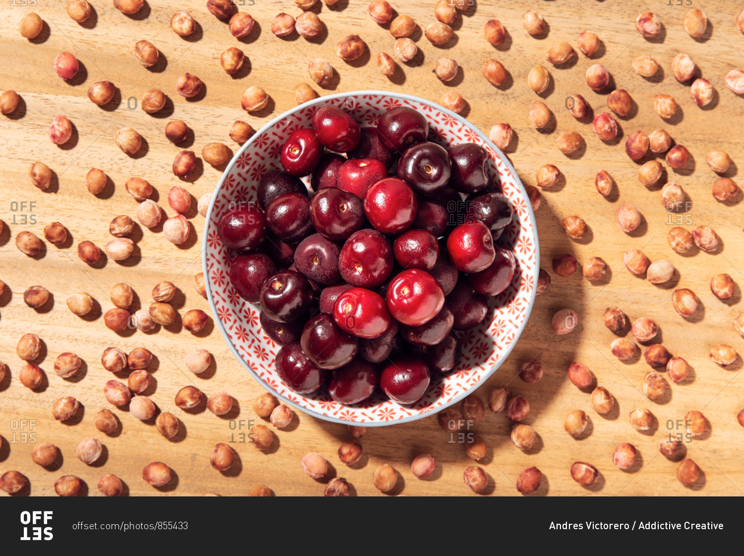 Top view of fresh sweet cherries in bowl with cherry seeds around on wooden table