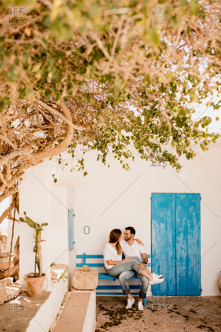 Smiling man and woman chilling on wooden bench in embrace at light patio in summer and looking at each other
