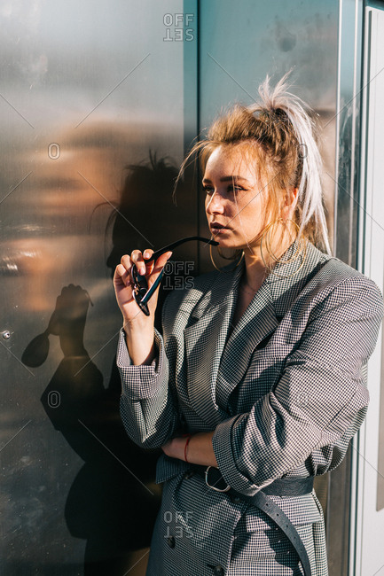 Fashion attractive woman with trendy hairstyle and sunglasses nearby dark shiny metal wall looking away