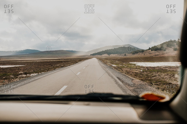 Asphalt road going through plains and hills in front of vehicle on gray overcast day in morocco