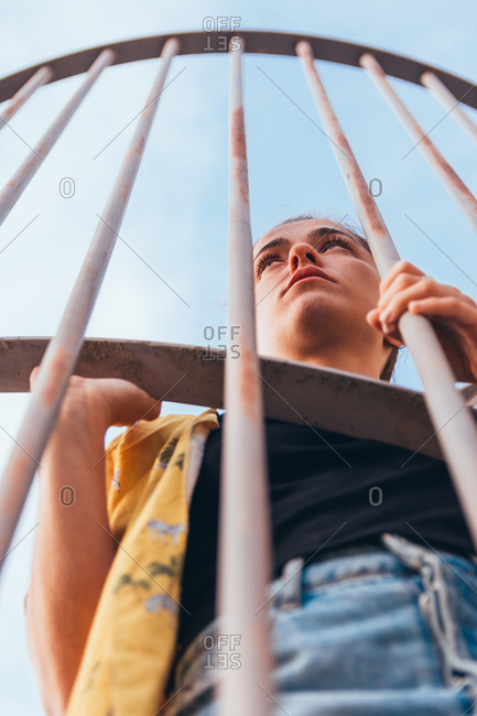From below sensual casual woman standing in cage on clear sky in summer and looking away