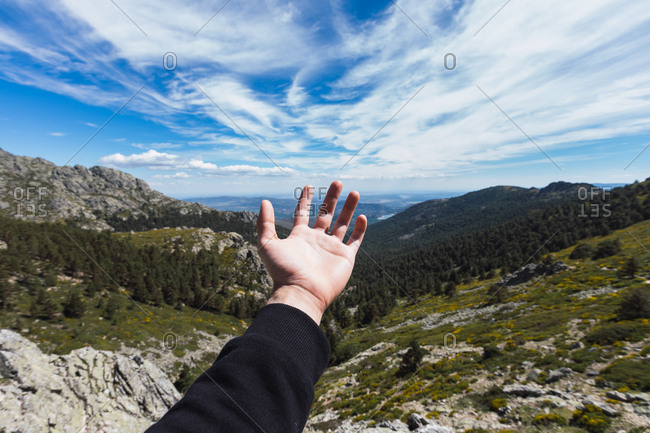 Hand of crop man stretching to blue cloudy sky forests and mountains