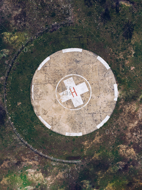 Drone top view of round concrete helipad on grassy rural valley on summer day