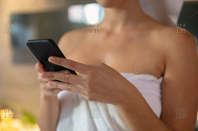 Mid section of a young Caucasian woman wearing a bath towel using a smartphone in a bathroom