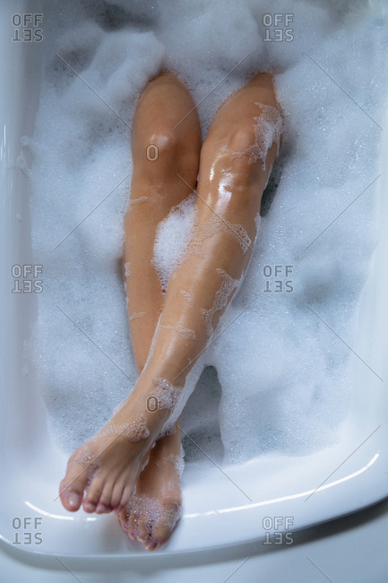 Close up the legs of a young Caucasian woman, raised up on the edge while she lies in a foam bath