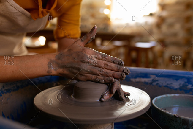 Close up of the hands of a young Caucasian female potter shaping wet clay on a potters wheel in a pottery studio