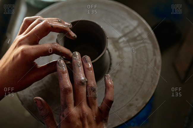 Elevated close up of the hands of a young Caucasian female potter shaping wet clay into a pot shape on a potters wheel in a pottery studio