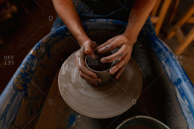 Elevated close up of the hands of a young Caucasian female potter shaping wet clay into a pot shape on a potters wheel in a pottery studio