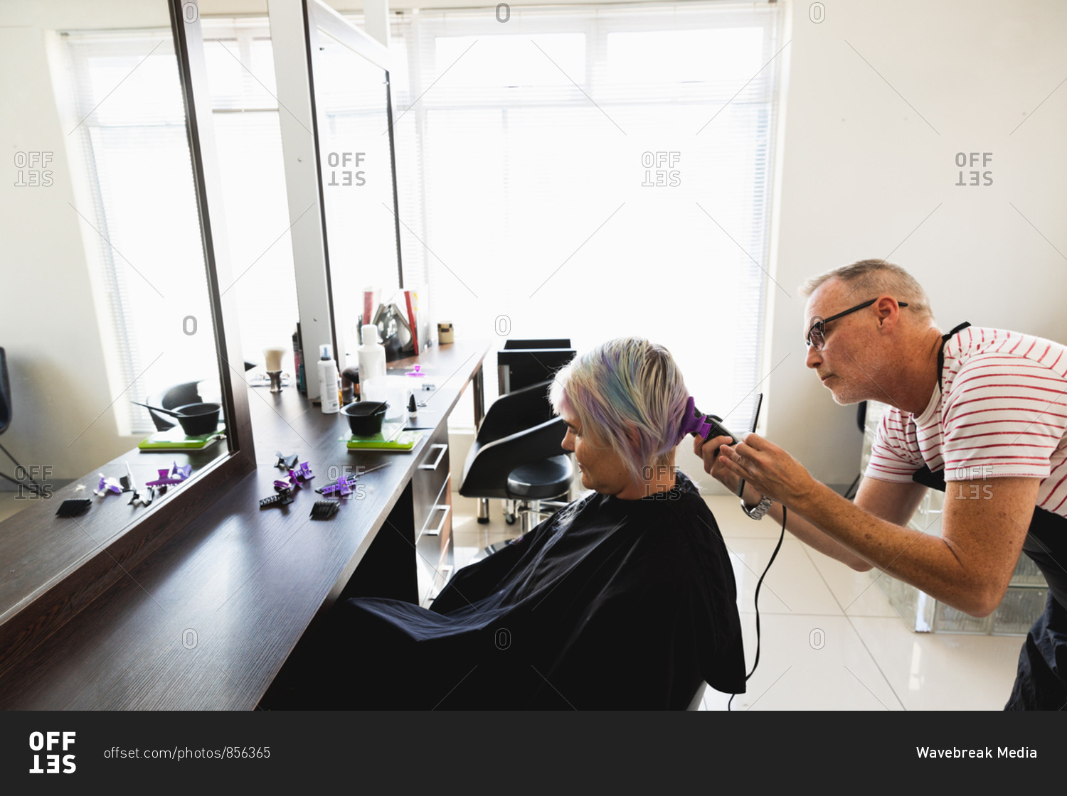 Side view of a middle aged Caucasian male hairdresser and a young Caucasian woman having her hair trimmed in a hair salon