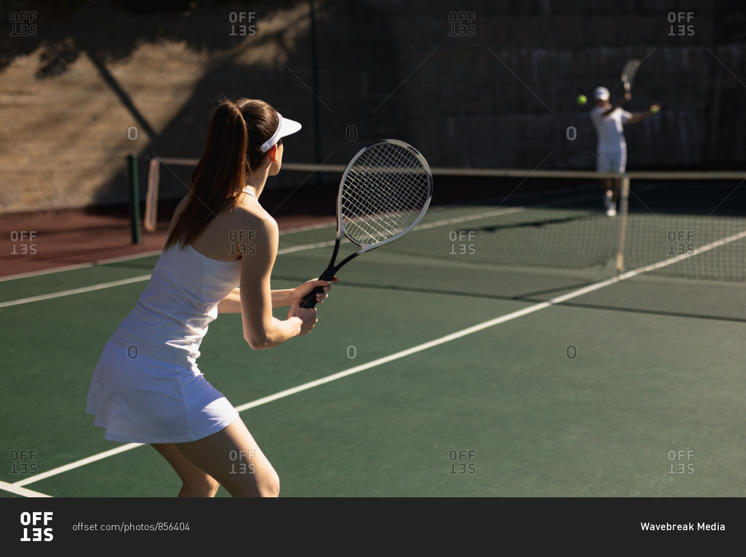 Rear view of a young Caucasian woman and a man playing tennis on a sunny day, man hitting a ball
