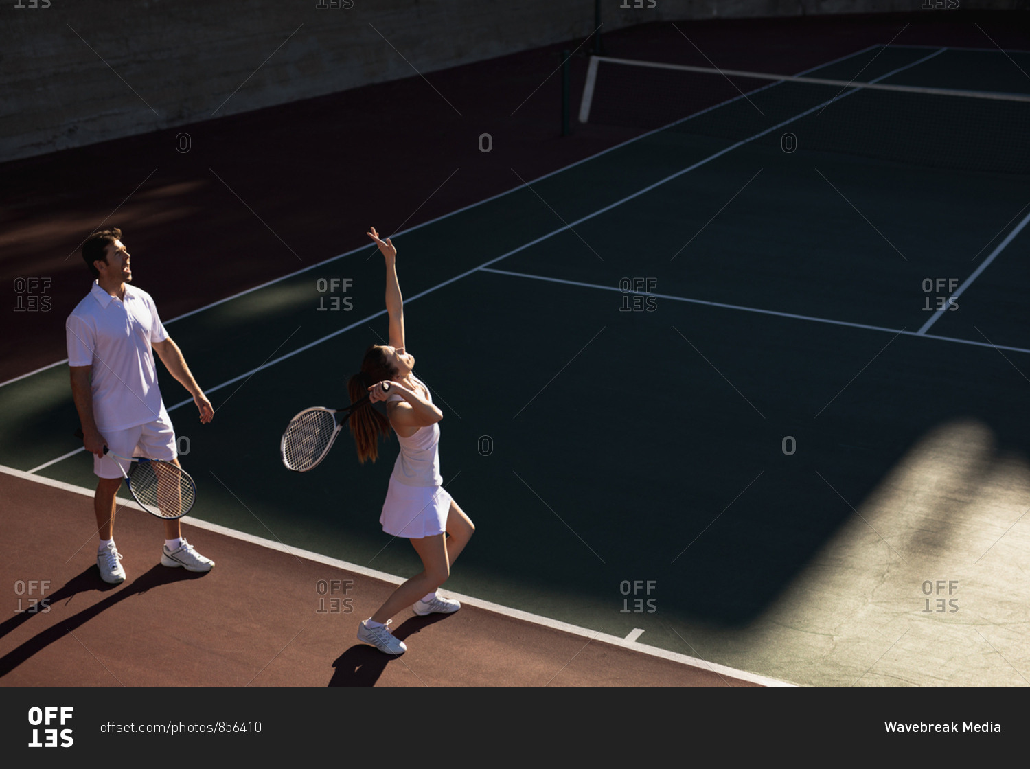 Side view of a young Caucasian woman and a man playing tennis on a sunny day, woman serving