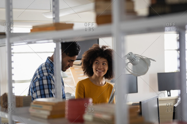 Side view of a young mixed race man and a young mixed race woman sitting at a desk having a discussion at a creative office