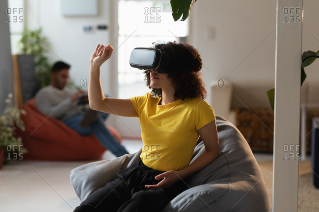 Front view of a young mixed race woman using a VR headset and a young mixed race man sitting in the background at a creative office