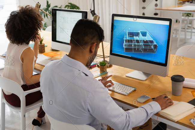Rear view close up of a young mixed race man and a young mixed race woman sitting at a desk using computers at a creative office