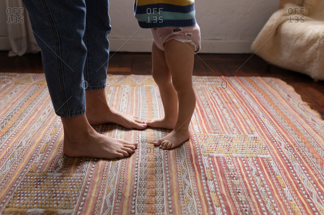 Side view of a low section of a young Caucasian mother standing on a carpet with her baby
