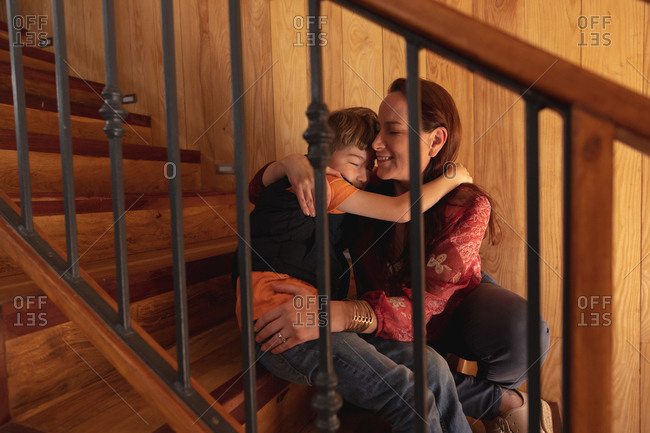 Front view close up of a middle aged Caucasian woman embracing with her pre teen son sitting on a staircase