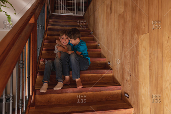 Portrait of two pre teen Caucasian boys sitting on a staircase at home, embracing and looking to camera