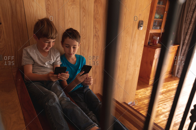 Front view close up of two pre teen Caucasian boys sitting on a staircase at home, using smartphones