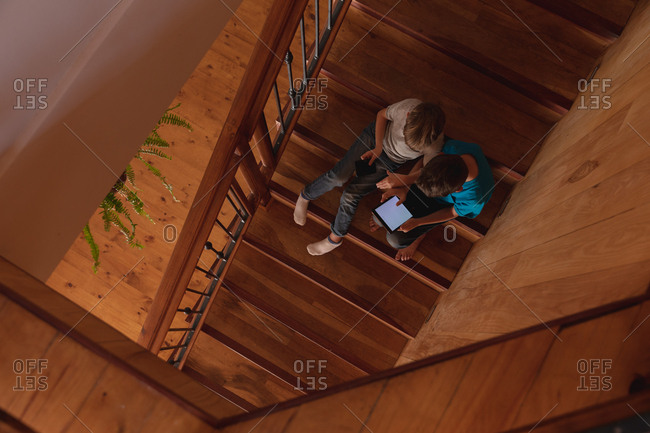Overhead view of two pre teen Caucasian boys sitting on a staircase at home, using a tablet computer and a smartphone