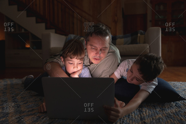 Front view of a middle aged Caucasian man and his pre teen sons using a laptop computer in a sitting room