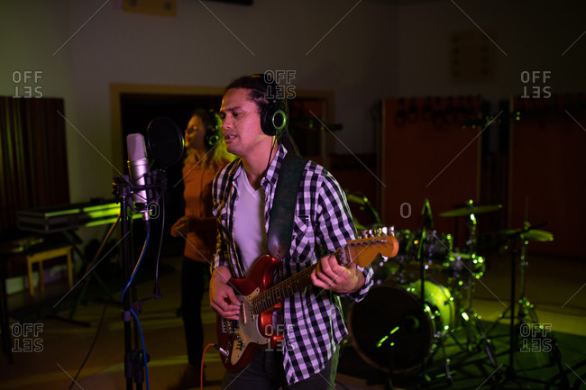 Side view of a young Caucasian female singer and a young mixed race male singer guitarist performing during a session at a recording studio