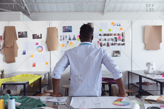 Rear view of a young African American male fashion student looking at drawings on the wall while working on a design looking at designs on a wall in a studio at fashion college