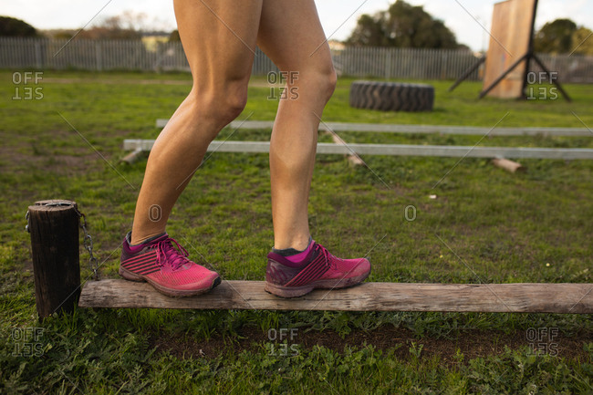 Side view low section of a young Caucasian woman walking along a wooden pole at an outdoor gym during a bootcamp training session