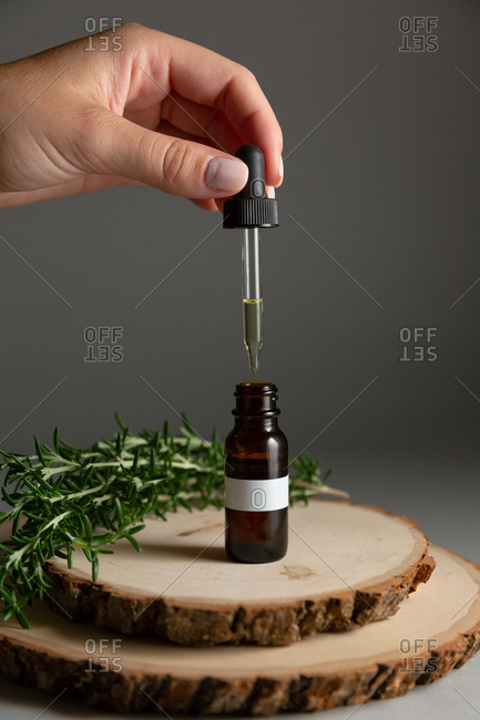 Hand holding dropper from essential oil bottle surrounded by rosemary