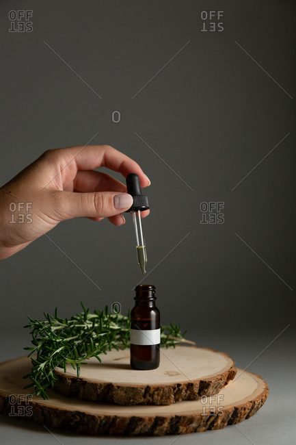 Hand placing dropper into essential oil bottle surrounded by rosemary